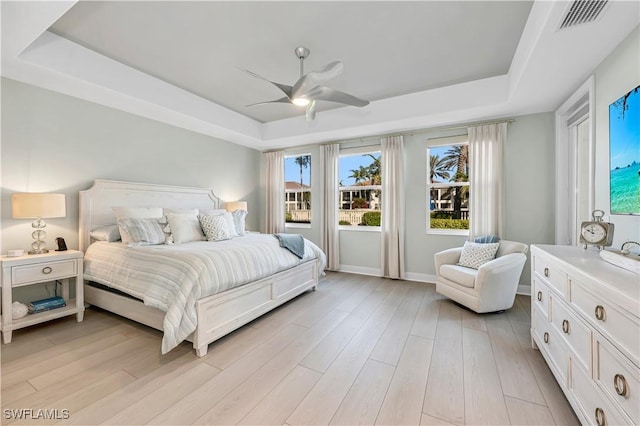 bedroom featuring ceiling fan, a raised ceiling, and light wood-type flooring