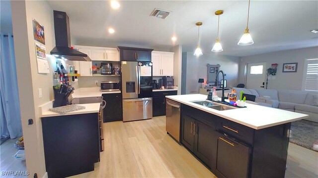 kitchen featuring pendant lighting, appliances with stainless steel finishes, an island with sink, white cabinets, and wall chimney exhaust hood