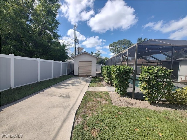 view of yard featuring an outbuilding, glass enclosure, a fenced backyard, a detached garage, and concrete driveway