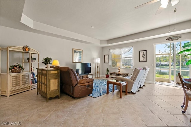 living room with light tile patterned floors, a tray ceiling, and ceiling fan