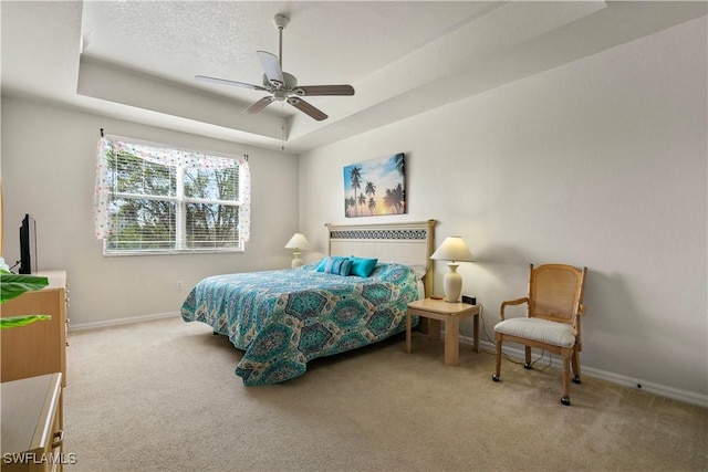 bedroom featuring a tray ceiling, a textured ceiling, ceiling fan, and carpet