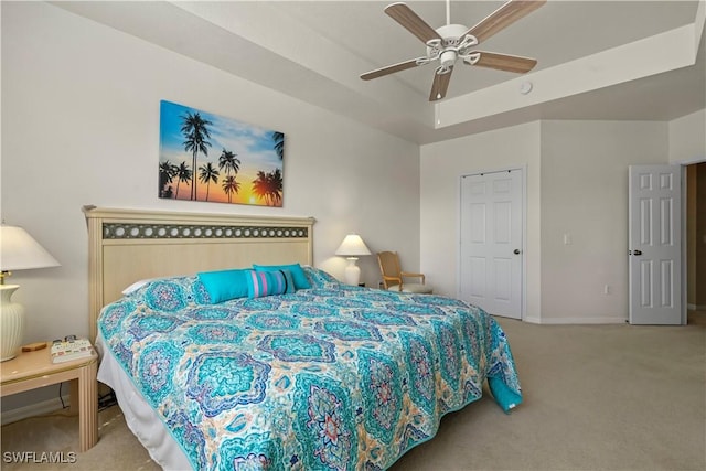 carpeted bedroom featuring ceiling fan and a tray ceiling