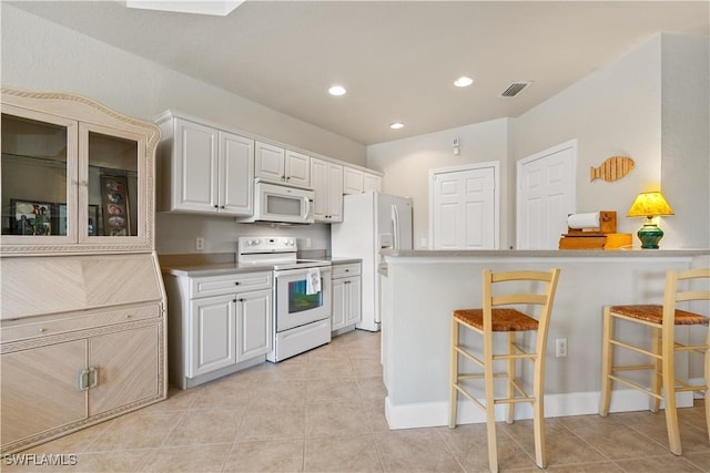 kitchen with light tile patterned floors, white appliances, white cabinets, and a kitchen bar