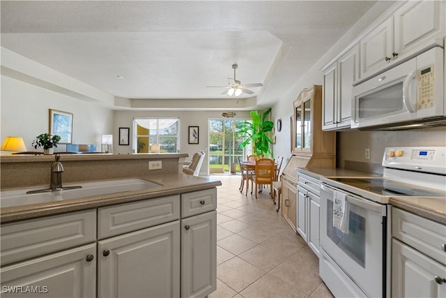 kitchen featuring light tile patterned flooring, sink, white cabinetry, a tray ceiling, and white appliances