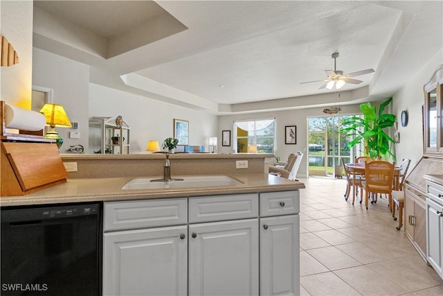 kitchen with light tile patterned floors, sink, white cabinetry, black dishwasher, and a raised ceiling