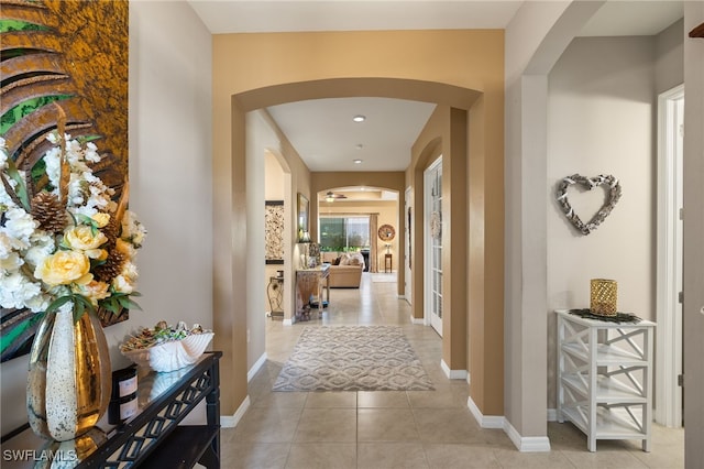 hallway featuring arched walkways, light tile patterned floors, and baseboards