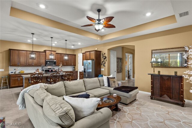 living room featuring arched walkways, light tile patterned flooring, ceiling fan, recessed lighting, and a raised ceiling