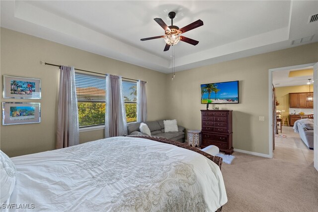 bedroom featuring a raised ceiling, light carpet, baseboards, and ceiling fan