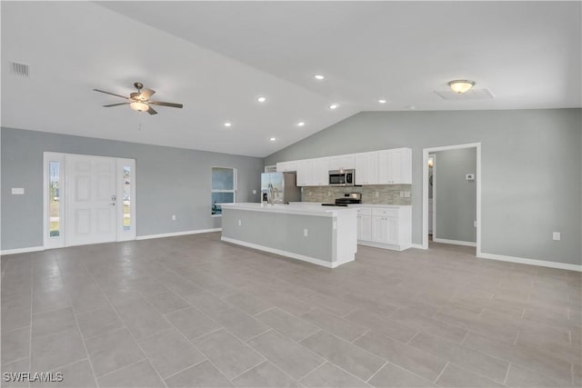 kitchen featuring lofted ceiling, white cabinets, decorative backsplash, stainless steel appliances, and a center island with sink