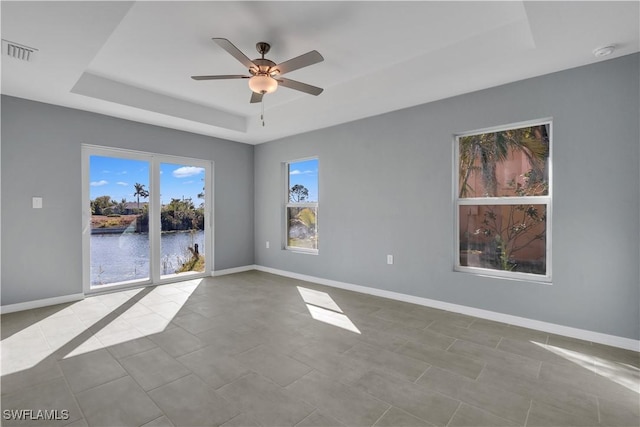 unfurnished room with light tile patterned floors, a tray ceiling, ceiling fan, and a water view