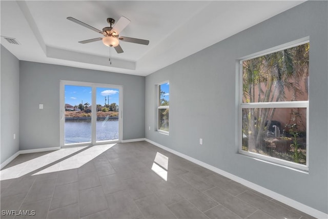 empty room featuring tile patterned floors, a raised ceiling, ceiling fan, and a water view