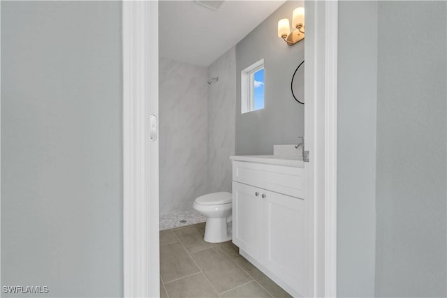 bathroom with tile patterned floors, vanity, toilet, and a tile shower