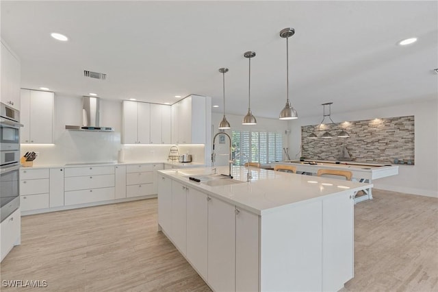 kitchen featuring a sink, white cabinets, light countertops, a large island, and wall chimney exhaust hood