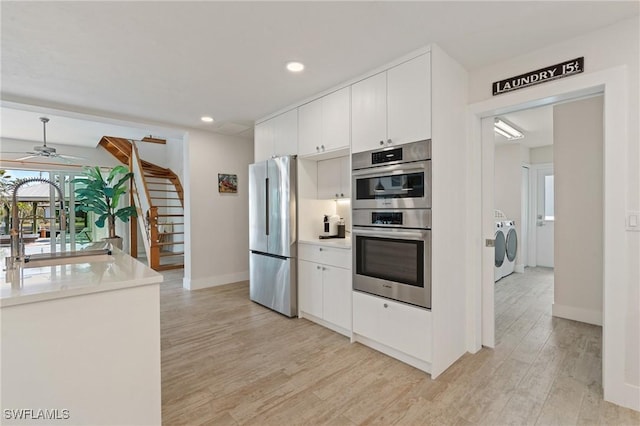 kitchen with stainless steel appliances, washing machine and dryer, white cabinets, and light countertops