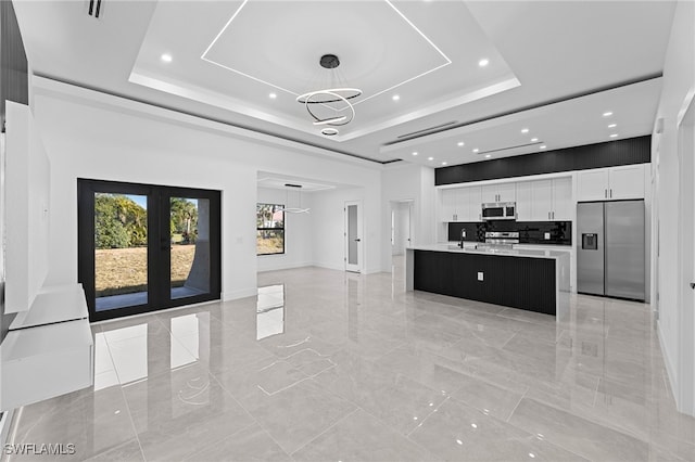 kitchen with a kitchen island, pendant lighting, a raised ceiling, white cabinets, and stainless steel appliances