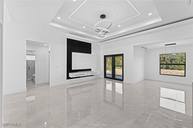 spare room featuring french doors, a notable chandelier, a tray ceiling, and a high ceiling