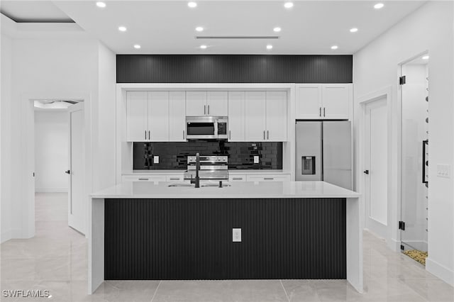 kitchen with sink, white cabinetry, appliances with stainless steel finishes, an island with sink, and backsplash