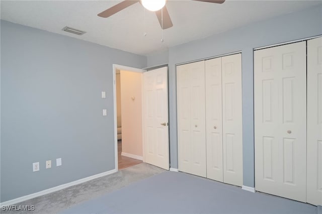 unfurnished bedroom with light carpet, two closets, and ceiling fan