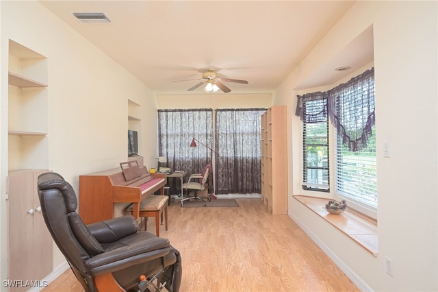 living area with built in features, ceiling fan, and light hardwood / wood-style flooring