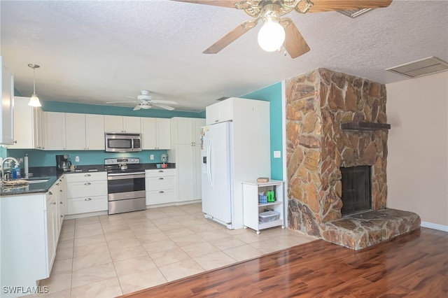 kitchen featuring appliances with stainless steel finishes, decorative light fixtures, sink, white cabinets, and light hardwood / wood-style flooring