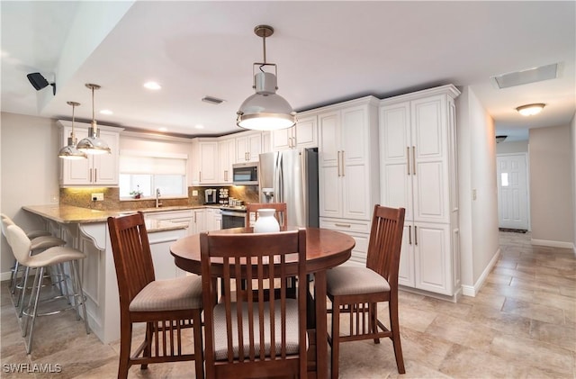 kitchen with white cabinets, hanging light fixtures, kitchen peninsula, stainless steel appliances, and light stone countertops