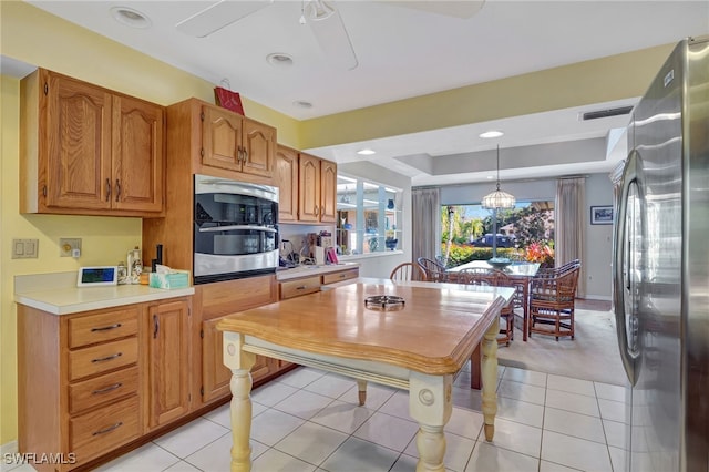 kitchen featuring light tile patterned flooring, pendant lighting, ceiling fan, a tray ceiling, and stainless steel appliances