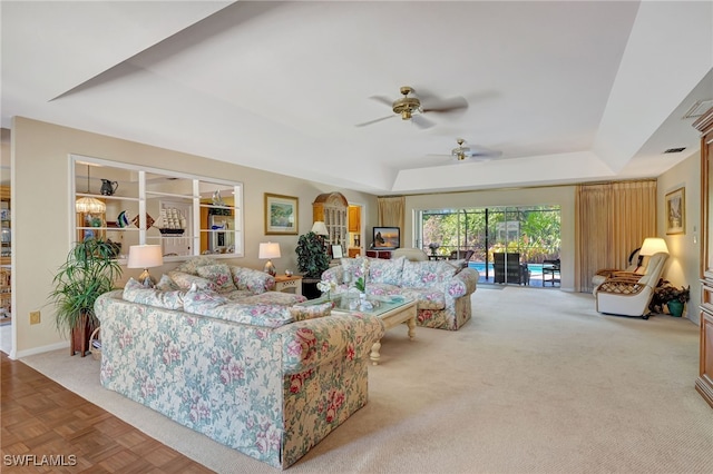 carpeted living room with ceiling fan and a tray ceiling