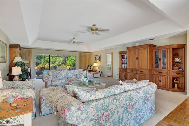 living room with a raised ceiling, light parquet flooring, and ceiling fan