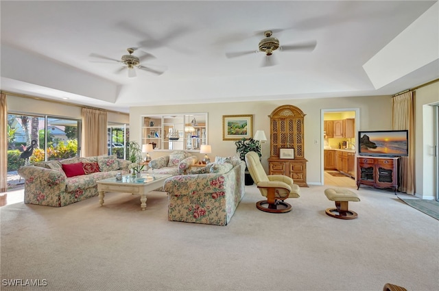 carpeted living room with a raised ceiling and ceiling fan