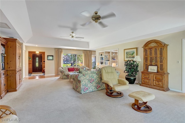 living room with built in shelves, light carpet, ceiling fan, and a tray ceiling