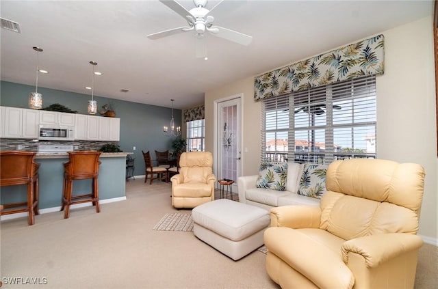 carpeted living room with ceiling fan with notable chandelier