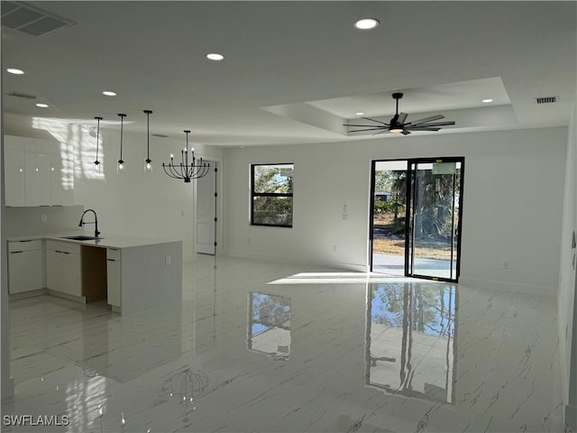 interior space with white cabinetry, sink, pendant lighting, and a raised ceiling