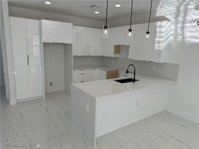 kitchen with sink, decorative light fixtures, kitchen peninsula, and white cabinets