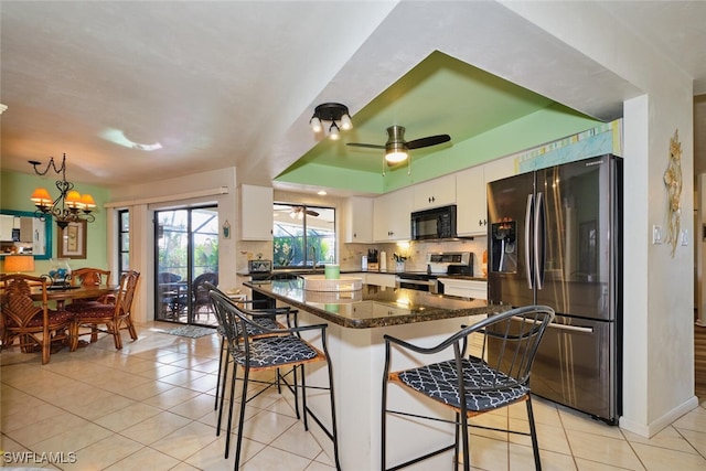 kitchen with stainless steel appliances, a kitchen breakfast bar, dark stone counters, and white cabinets