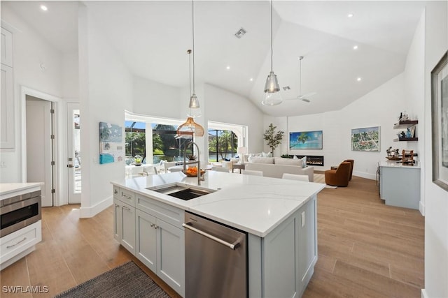 kitchen with sink, appliances with stainless steel finishes, high vaulted ceiling, an island with sink, and decorative light fixtures