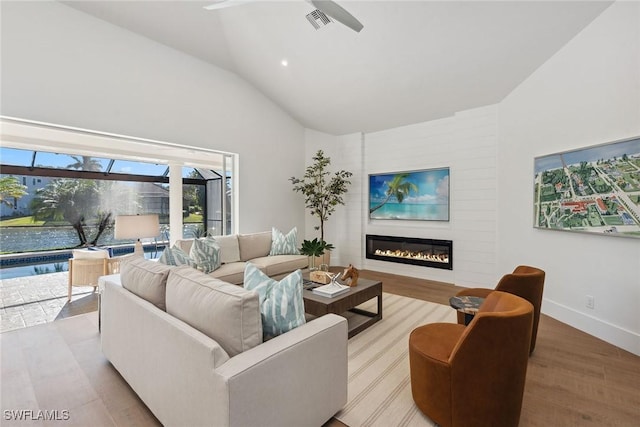 living area featuring a glass covered fireplace, ceiling fan, vaulted ceiling, wood finished floors, and baseboards