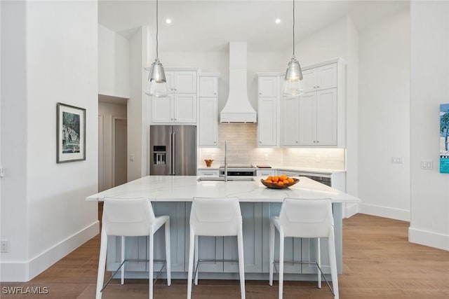 kitchen featuring baseboards, stainless steel refrigerator with ice dispenser, premium range hood, a kitchen breakfast bar, and decorative backsplash