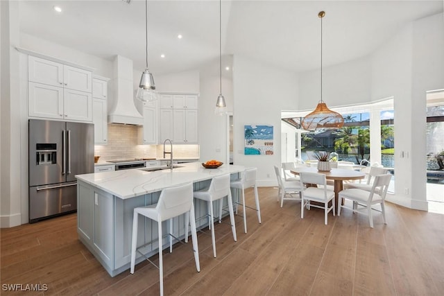 kitchen featuring high vaulted ceiling, custom exhaust hood, a sink, and high end fridge