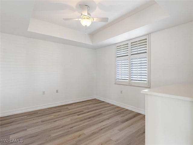 unfurnished room with a tray ceiling, ceiling fan, and light hardwood / wood-style floors