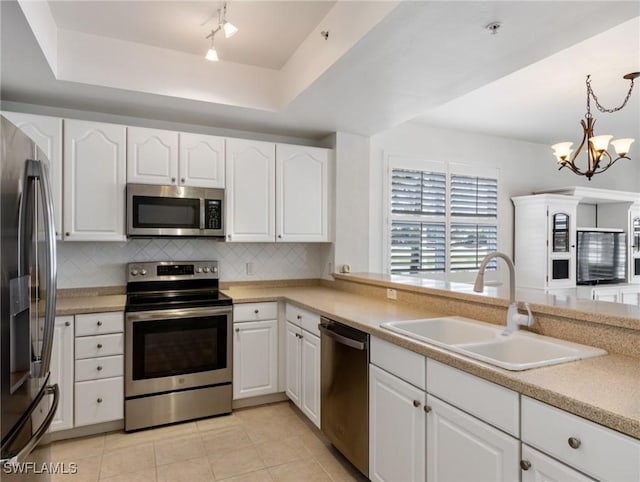 kitchen with appliances with stainless steel finishes, sink, white cabinets, hanging light fixtures, and tasteful backsplash