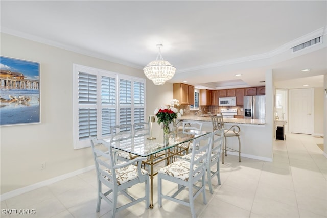 tiled dining space featuring an inviting chandelier, ornamental molding, and a raised ceiling