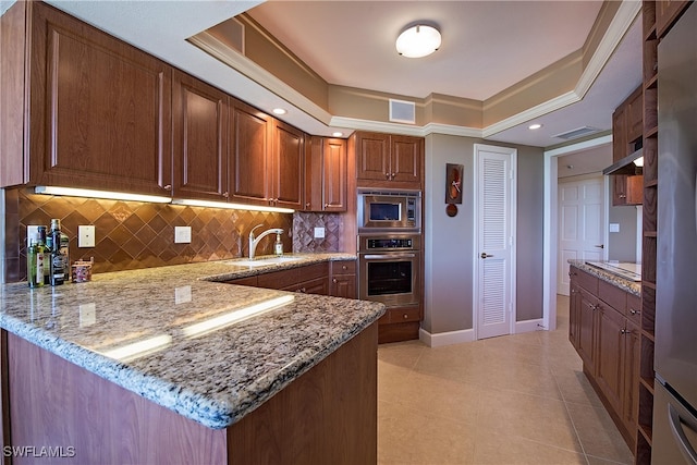 kitchen with a raised ceiling, appliances with stainless steel finishes, light stone counters, and kitchen peninsula