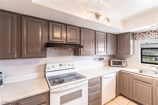 kitchen with a sink, under cabinet range hood, white appliances, and light countertops