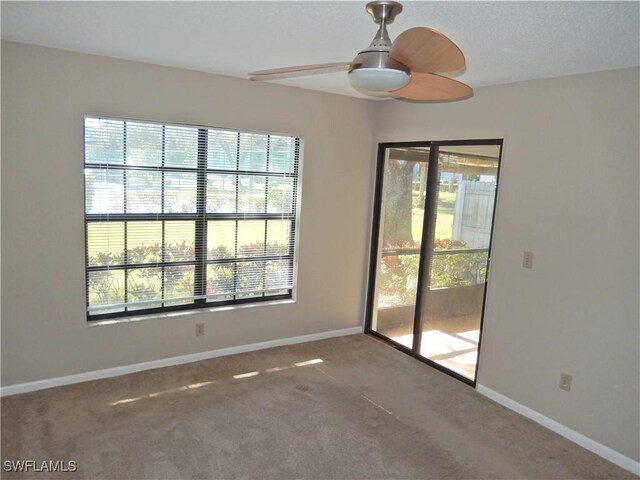 carpeted spare room with a ceiling fan, a wealth of natural light, and baseboards