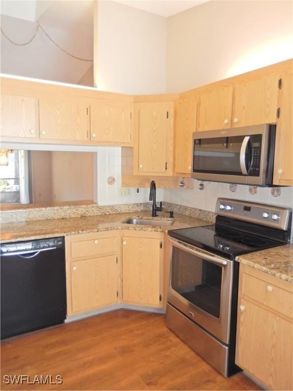 kitchen with stainless steel appliances, light brown cabinetry, a sink, light stone countertops, and light wood-type flooring