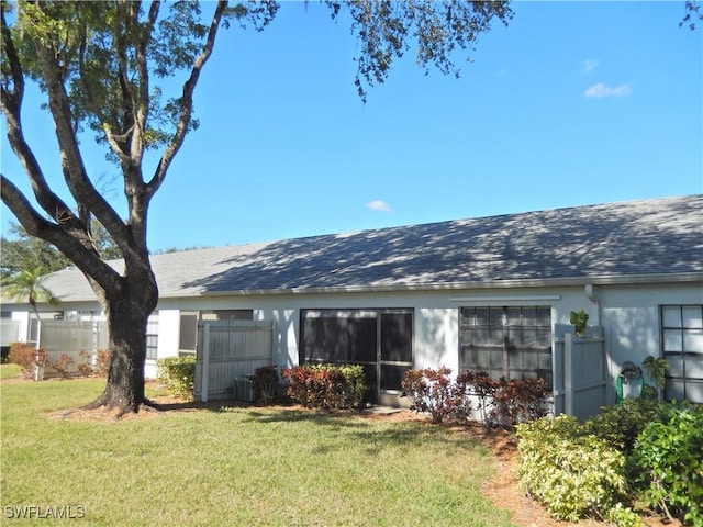 rear view of property with a yard, a shingled roof, fence, and stucco siding