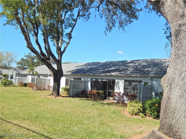 rear view of property featuring stucco siding, fence, and a lawn