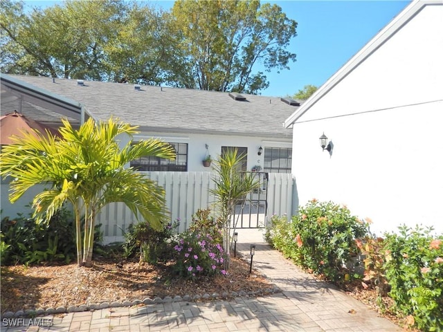 entrance to property featuring stucco siding, fence, and a shingled roof