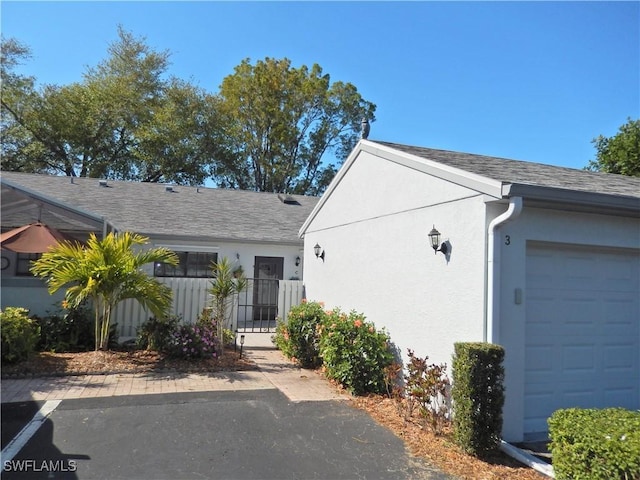 view of front of home featuring fence, roof with shingles, stucco siding, an attached garage, and a gate