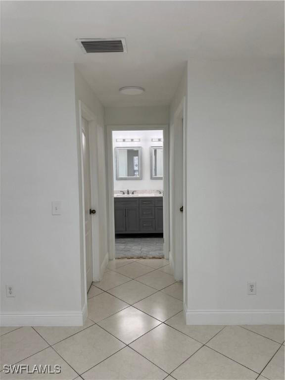 hallway featuring visible vents, a sink, baseboards, and light tile patterned flooring